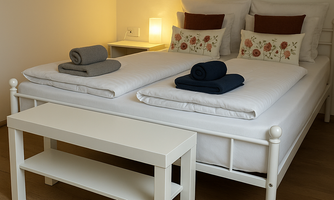A cozy bedroom with two beds and colorful cushions. A small table and towels provide extra comfort.