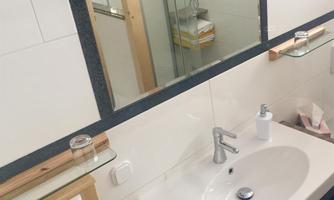 A modern bathroom with a sink, mirror, and wooden details. In the background, towels and a shower are visible.