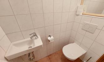 A small bathroom with white tiles and a modern sink. To the right is a toilet and a mirror.