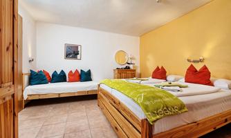 A cozy hotel room with wooden furniture and colorful cushions. The walls are yellow, and there are two beds as well as a dressing table.