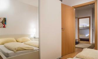 A cozy bedroom with a bed and bright pillows. In the background, another room with a bunk bed can be seen.