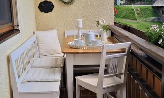A cozy balcony with a small table and two chairs. The surroundings are green and inviting, ideal for relaxed hours outdoors.