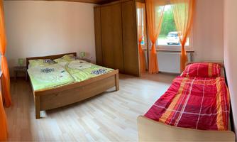 A cozy bedroom with two beds and orange curtains. The room has a wooden floor and windows that let in natural light.