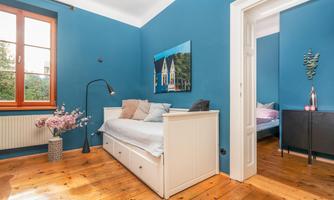 A modern bedroom with blue walls and hardwood floor. The room features a daybed, a floor lamp, and a window with a view.