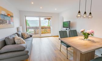 A bright living room with a cozy sofa and a dining table. Large windows offer a view of the terrace with plenty of natural light.