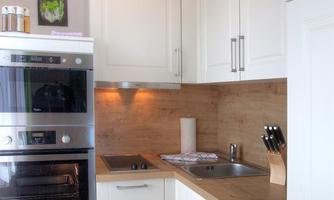 A modern kitchen with white cabinets and wooden details. There is an oven, a sink, and a stove top.