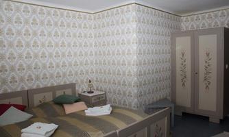 A cozy bedroom with a large bed and floral wallpaper. The room includes a wardrobe and decorative cushions.