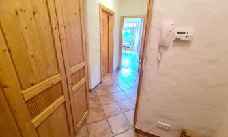 An inviting hallway with wooden cabinets and tiled flooring. A bright living space is visible through a door.
