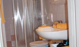 A small bathroom with a shower cabin, sink, and mirror. Towels and toiletries are neatly organized.
