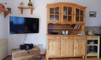 A cozy living room with a television and a wooden cabinet. There is also seating and decorative elements on the wall.