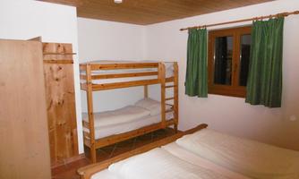 A simple bedroom with a bunk bed and a double bed. The walls are white, and there are green curtains at a window.
