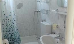 A small bathroom with white tiles and a shower curtain in shades of blue and green. It contains a toilet, a sink, and a shower.