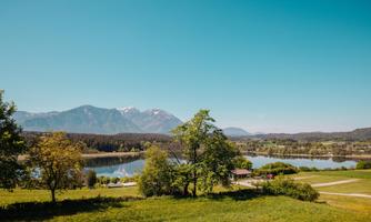 A beautiful landscape with a peaceful lake and green meadows. In the background, majestic mountains and a clear blue sky can be seen.
