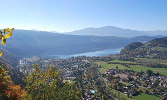 A picturesque landscape with a clear lake and gentle hills. In the foreground, green meadows and trees can be seen.