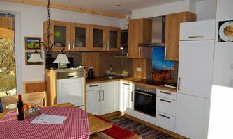 A modern kitchen with light wood cabinets and white elements. A dining table with red tablecloths and a few decorative items are also visible.