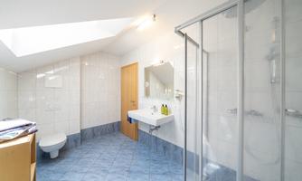 A modern bathroom with a shower and window for daylight. The walls are tiled in light colors and there is a wash area with a mirror.
