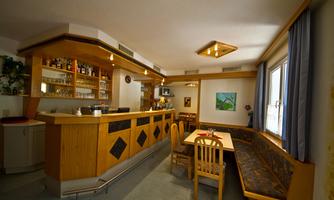 A cozy room with a wooden bar and a seating area. Bright walls and a window create a pleasant atmosphere.