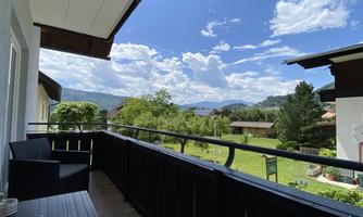 A balcony with a beautiful view of the countryside and the sky. The sun is shining and there are a few clouds visible.