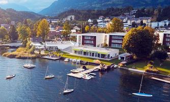 A picturesque lake with sailing boats and a modern building on the shore. In the background, gentle hills and a wooded landscape can be seen.