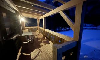 A cozy terrace with wooden paneling, illuminated by a lamp. The snow outside creates a tranquil winter atmosphere.