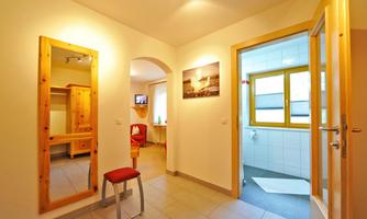 A bright hallway with a large mirror and a red chair. In the background, a bathroom with a window is visible.