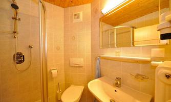 A small bathroom with a shower, sink, and toilet. The room has bright tiles and a wooden ceiling.