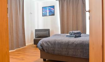 A modern bedroom with a comfortable bed and an armchair. The walls are painted in neutral tones, and a picture hangs on the wall.