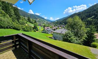 A beautiful view from a balcony overlooking a picturesque valley. Green meadows and mountains surround a small village with houses.