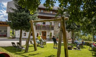 A large garden with a swing and a cozy atmosphere. In the background, there is a beautiful house and some people are enjoying their time outdoors.