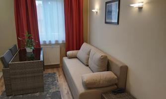 A cozy living room with a beige sofa and a modern table. Red curtains and soft lighting create an inviting atmosphere.