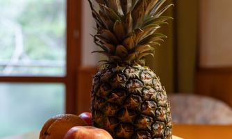 A selection of fresh fruits on a table. In the middle is a pineapple, surrounded by apples, a banana, and strawberries.