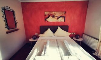 A cozy bedroom with a bed and decorative pillows. A painting hangs on the wall, and there is a mirror as well as small nightstands.