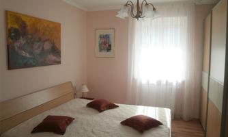 A cozy bedroom with a double bed and red pillows. The walls are painted in soft colors, and there is plenty of daylight coming through the window.