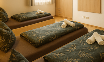A cozy sleeping room with three beds decorated with green bedspreads and fresh towels. The room has large windows that let in natural light.