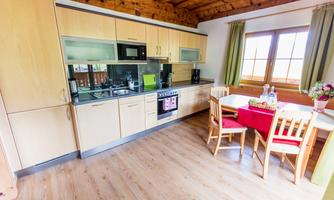 A modern kitchen with wooden furniture and green curtains. A table with chairs invites you to eat.
