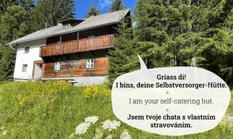 A cozy self-catering cabin surrounded by green meadows and trees. The sky is clear and the landscape is peaceful.