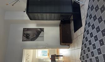 A modern entrance area with a black shoe cabinet and a designer coat rack. A poster of Vogue is hanging on the wall.
