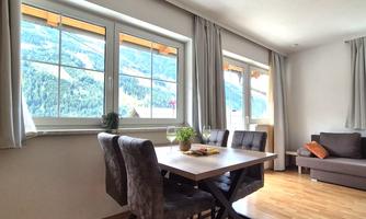 A bright living space with a dining table and chairs. Large windows offer a view of the mountains and nature.