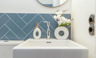 A modern bathroom with a white sink and stylish fixtures. A blue tile in a zigzag pattern and an orchid in a vase create an elegant atmosphere.