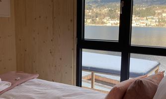 A cozy bedroom with a view of a lake and mountains. The bright walls and soft colors create a relaxed atmosphere.