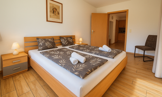 A bright bedroom with a large double bed and two nightstands. The cozy decor is complemented by warm wood tones and decorative cushions.