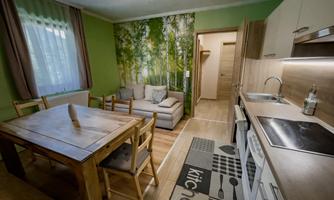 A modern kitchen with a wooden dining table and a cozy sofa. The walls are in soft green tones and decorated with a forest motif.