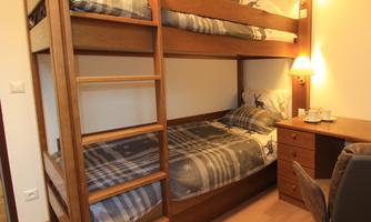 A cozy room with a wooden bunk bed. There is a desk and a lamp for extra light.