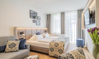 A modern bedroom with two beds and bright curtains. There is a cozy seating area and decorative pictures on the wall.