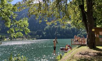 A picturesque lake surrounded by trees and mountains. People are enjoying the sun and the water on a dock.