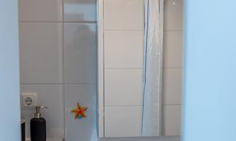 A modern bathroom with a white vanity unit and a large mirror. An orange star is attached to the wall.