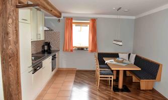 A modern kitchen with wooden details and a cozy dining area. The windows are adorned with orange curtains and the floor is made of wood.