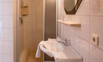 A modern bathroom with a shower and a sink. The walls are tiled in light colors and a mirror is mounted above the sink.
