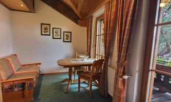 A cozy room with a table, chairs, and a sofa. Through the window, one can see a green landscape.