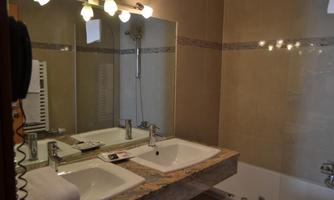A modernly furnished bathroom with two sinks and a large mirror. In the background, a bathtub can be seen.